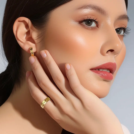 Close-up of a woman wearing gold earrings and a ring, with a neutral background