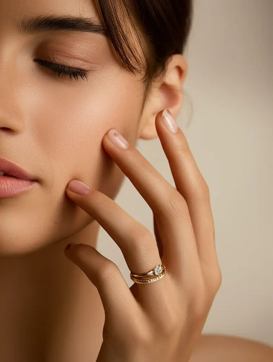 Close-up of a woman's hand with a ring on her finger, touching her face.