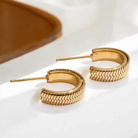Gold hoop earrings on a white surface with a brown object in the background