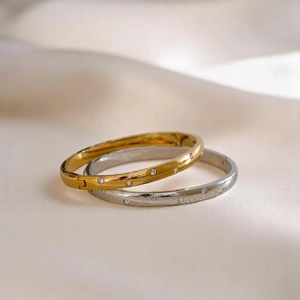 Two gold and silver bracelets with small diamonds on a light background
