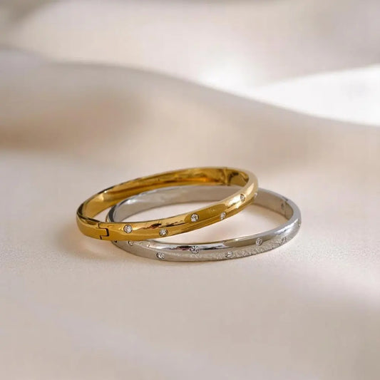Two gold and silver bracelets with small diamonds on a light background