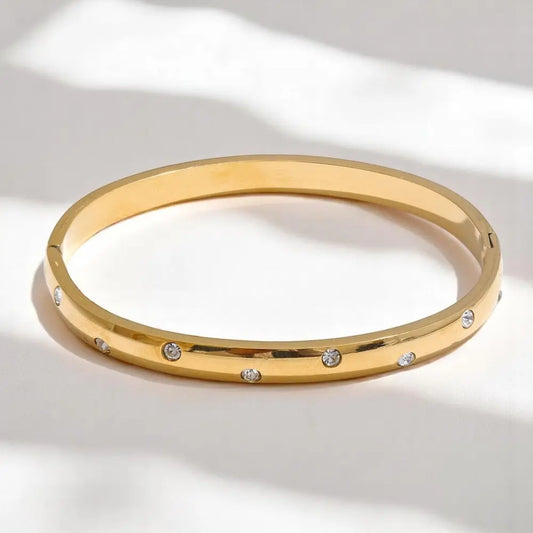 Gold bangle with embedded stones on a light background