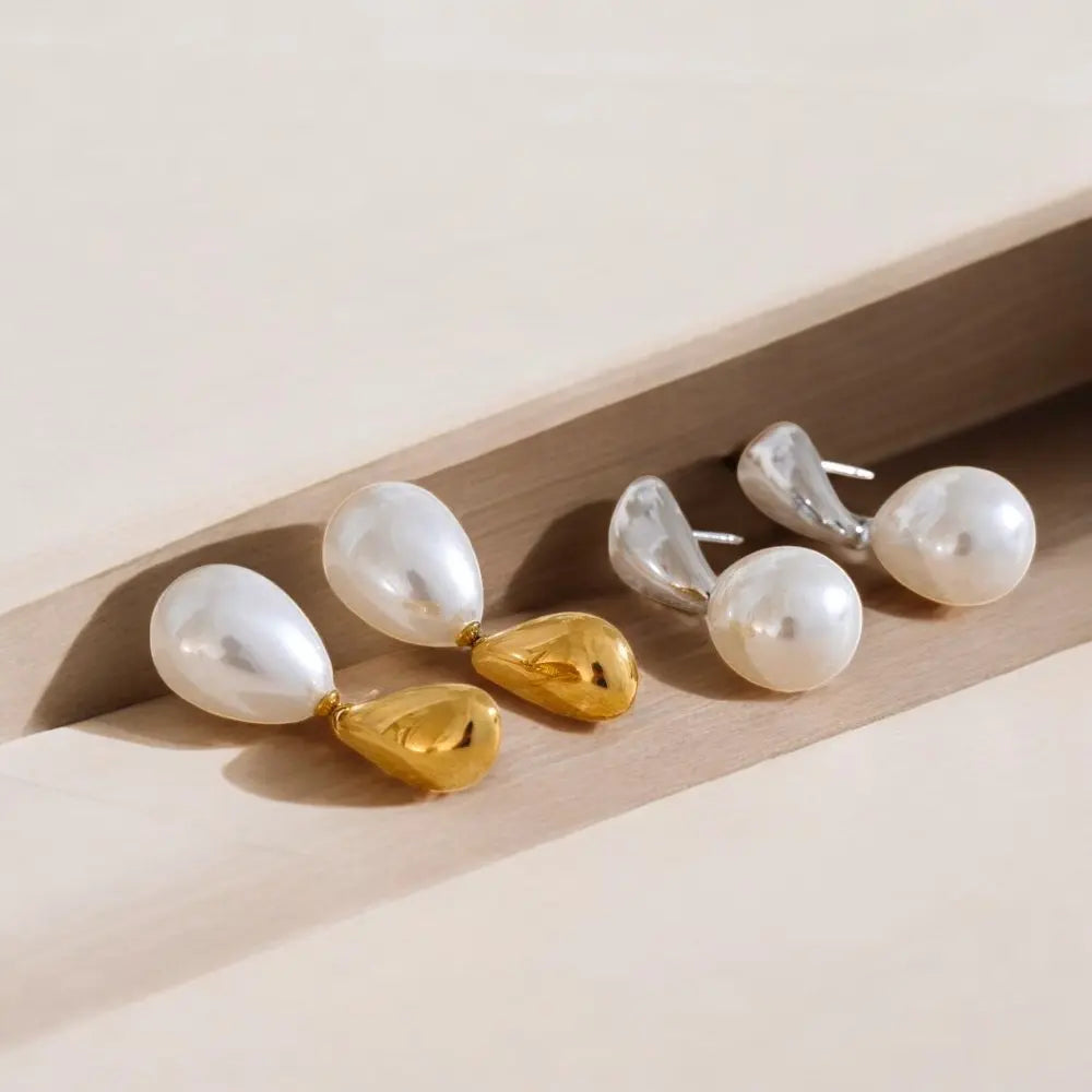 Pair of pearl earrings with gold and silver accents on a light wooden surface.