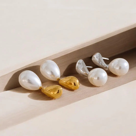 Pair of pearl earrings with gold and silver accents on a light wooden surface.