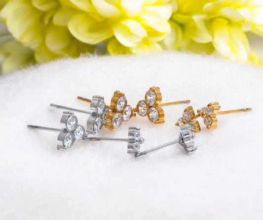 Set of bow-shaped earrings in gold and silver on a white surface with yellow flowers in the background