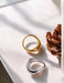 Two rings, one gold and one silver, on a light surface with a pine cone.