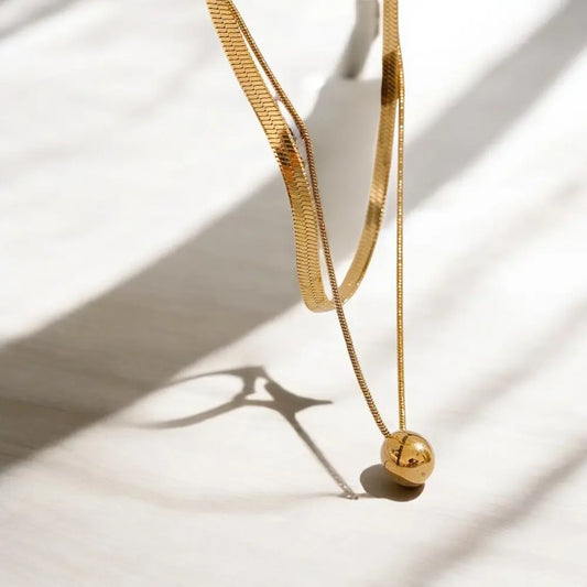Gold necklace with a spherical pendant on a light background