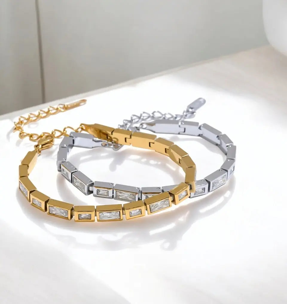 Gold and silver bracelet set on a reflective surface with a neutral background