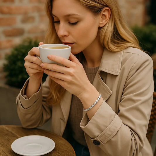 Woman in a beige coat drinking from a white cup outdoors.