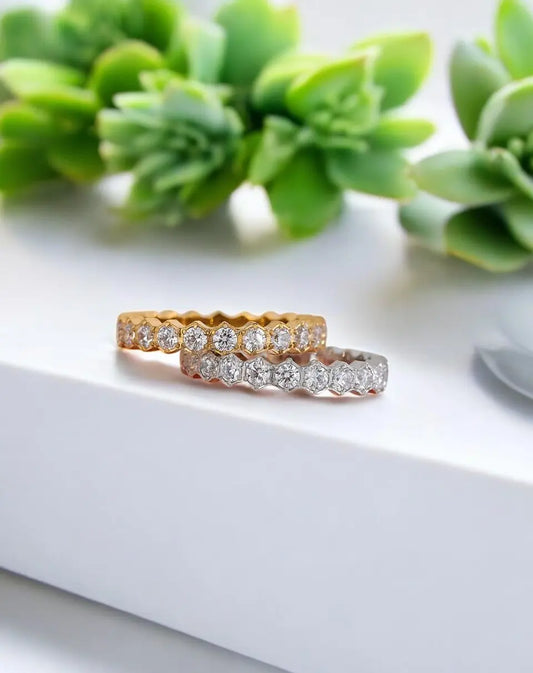Two diamond rings on a white surface with green succulents in the background