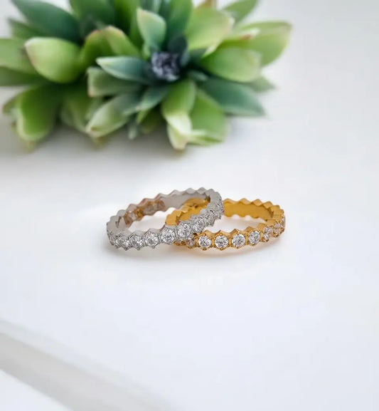 Two diamond-studded rings on a white surface with a green plant in the background