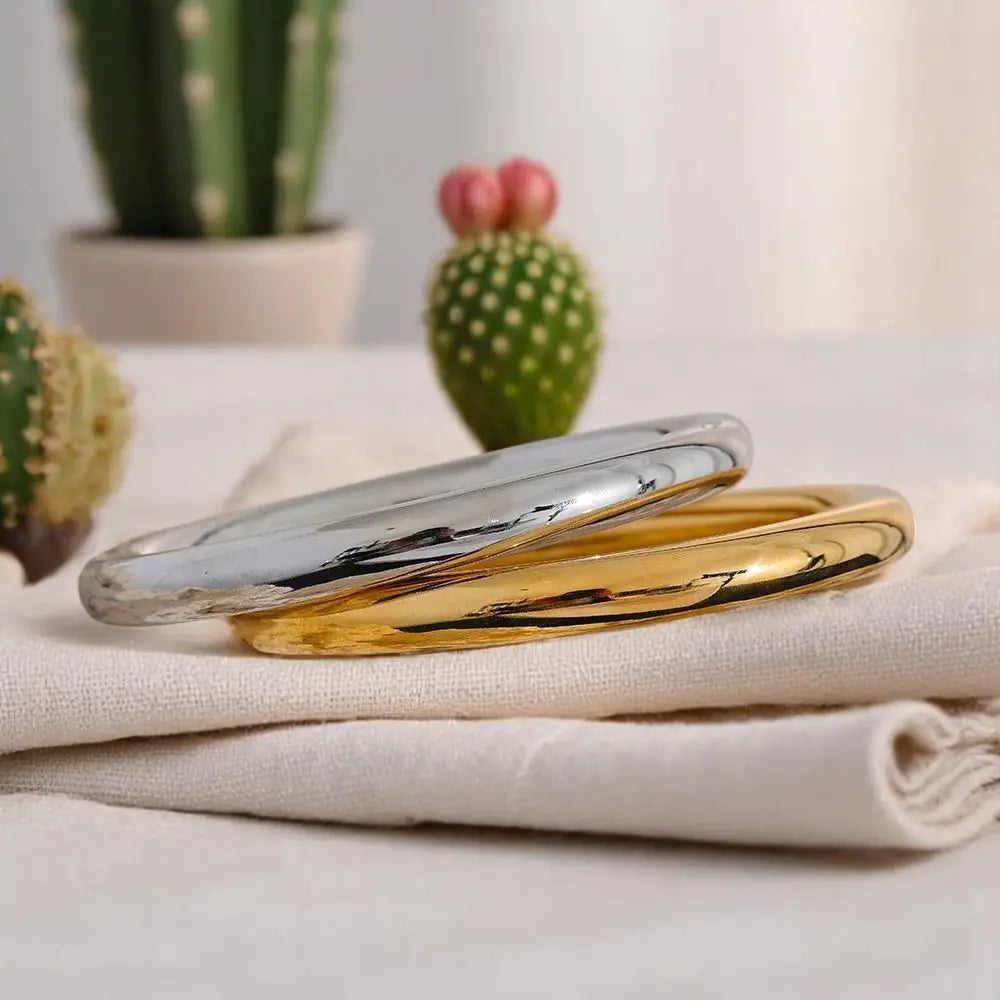 Two gold bangles on a white fabric surface with cacti in the background