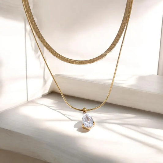 Gold necklace with a teardrop-shaped pendant on a light background
