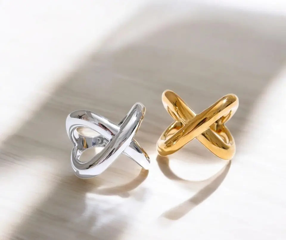 Two rings, one silver and one gold, on a reflective surface.