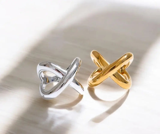 Two rings, one silver and one gold, on a reflective surface.