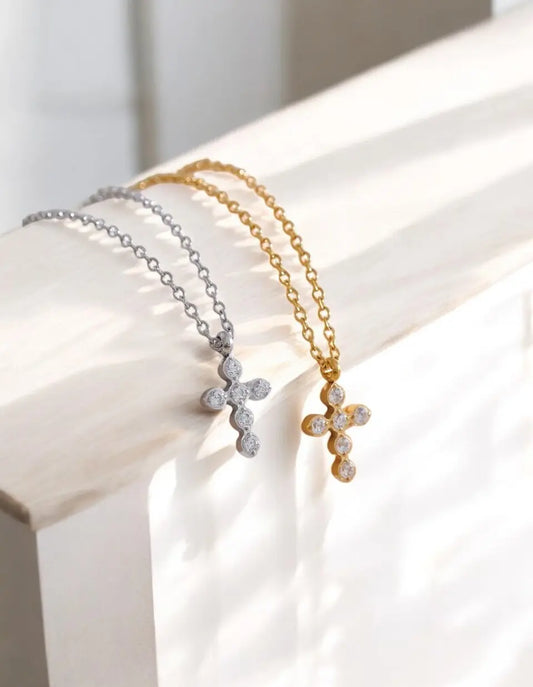 Two necklaces with cross pendants, one gold and one silver, on a white surface.
