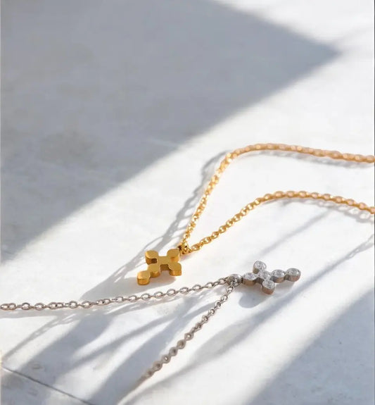 Two gold necklaces with a cross pendant on a light surface