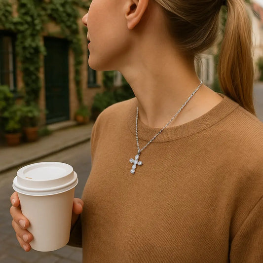Woman holding a coffee cup with a necklace featuring a cross pendant.