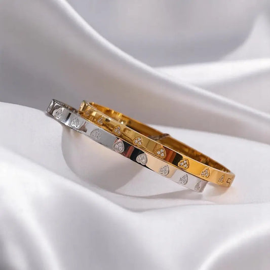 Three gold bracelets with diamond accents on a white fabric background