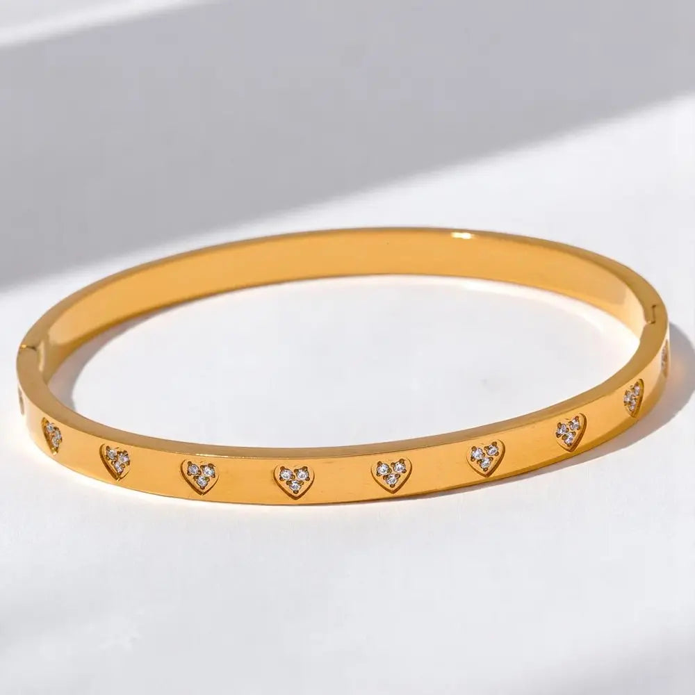 Gold bracelet with heart-shaped cutout stones on a light background