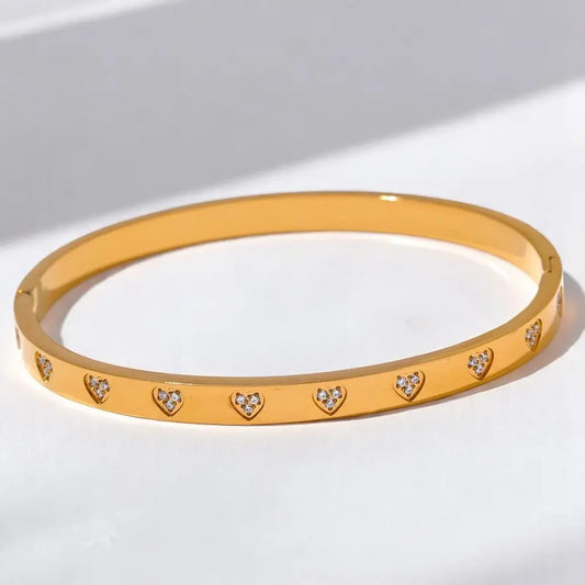 Gold bracelet with heart-shaped cutout stones on a light background