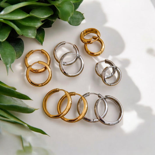 Gold and silver hoop earrings on a light surface with green leaves.