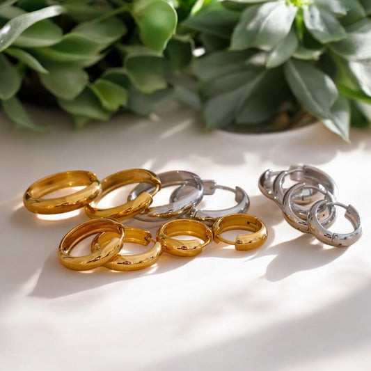 Gold and silver rings on a white surface with green plants in the background