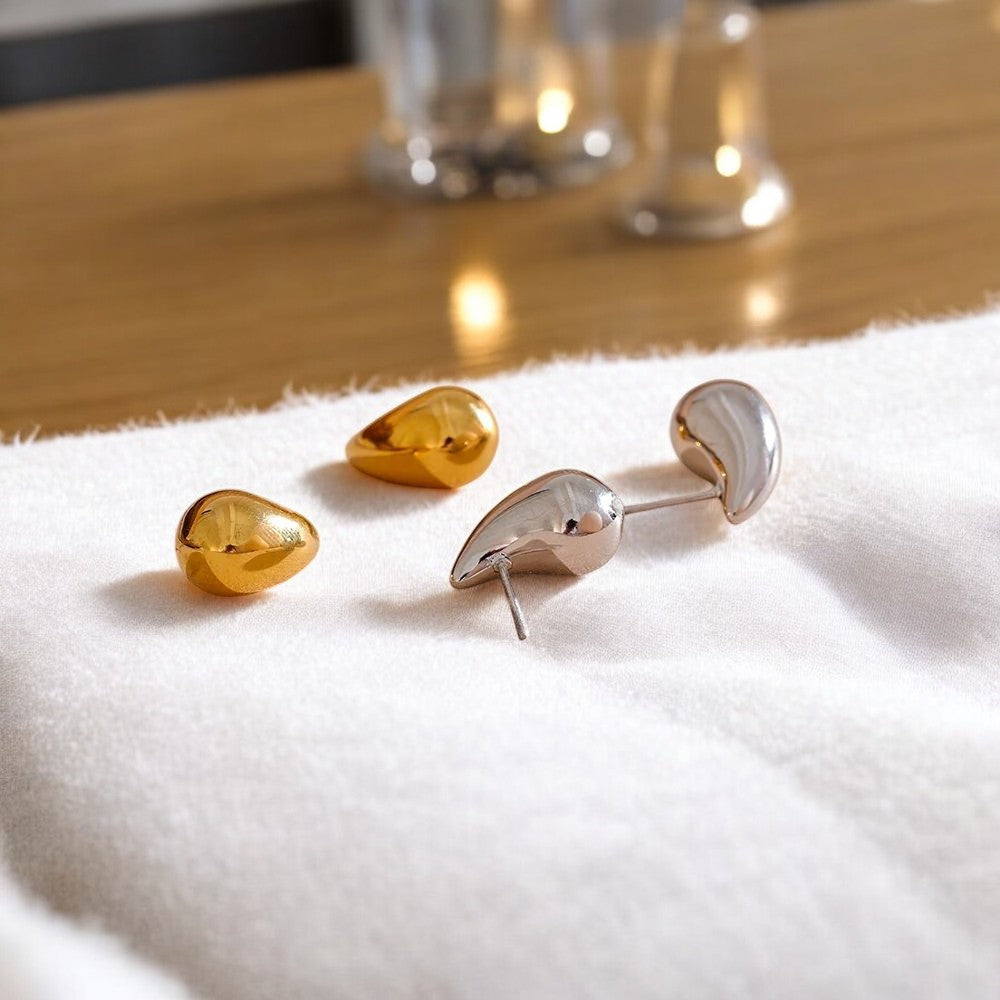 Gold and silver earrings on a white cloth with a blurred glass container in the background.
