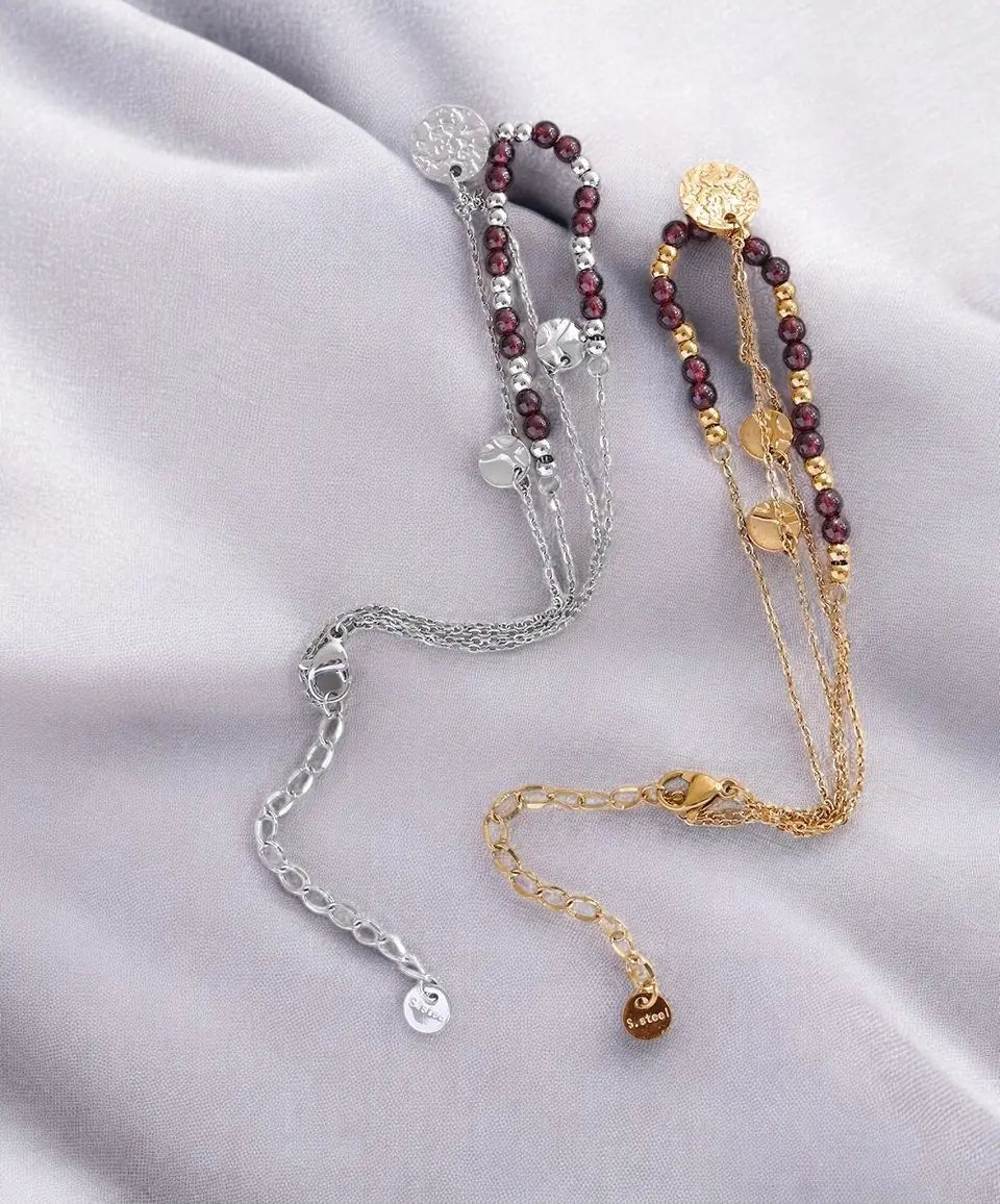 Three bracelets in silver, gold, and red on a light gray fabric background