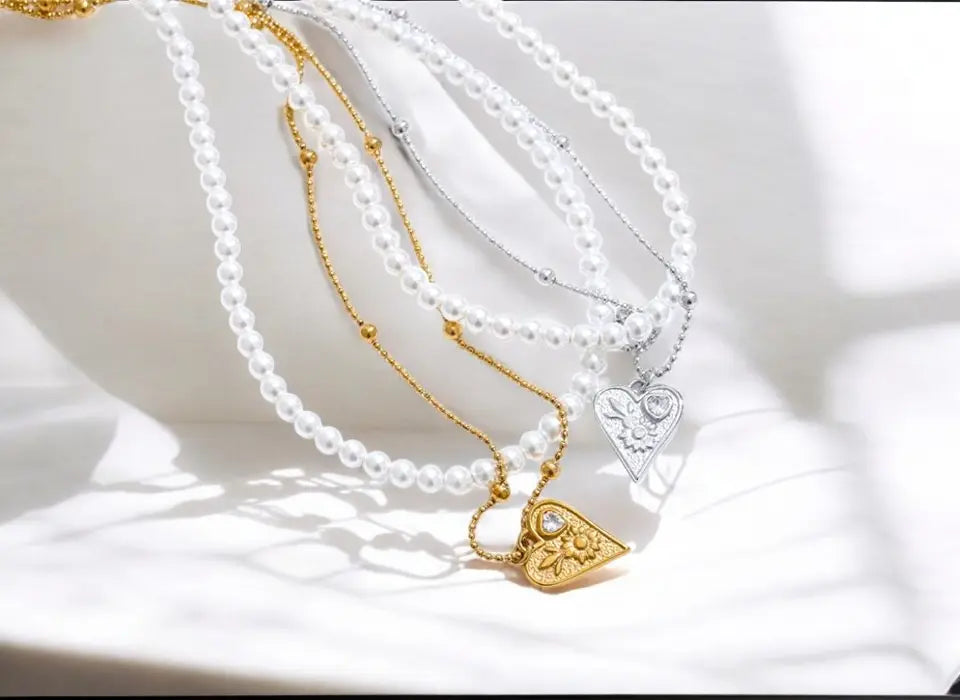 Two pearl necklaces with gold pendants on a white surface