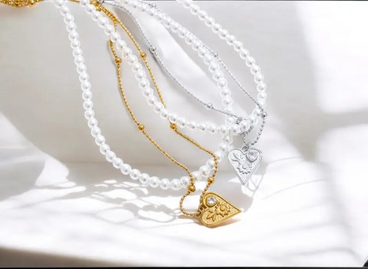 Two pearl necklaces with gold pendants on a white surface