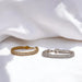 Two bracelets, one gold and one silver, on a white fabric background