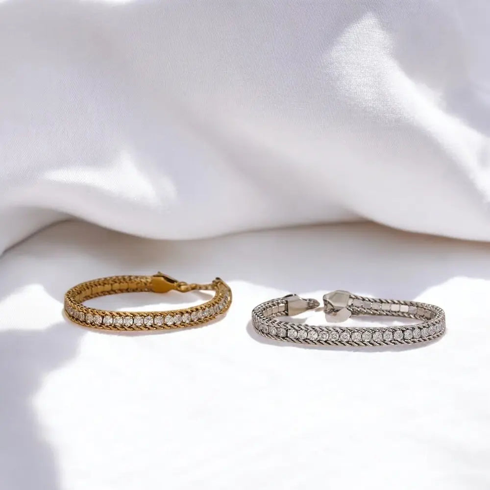 Two bracelets, one gold and one silver, on a white fabric background