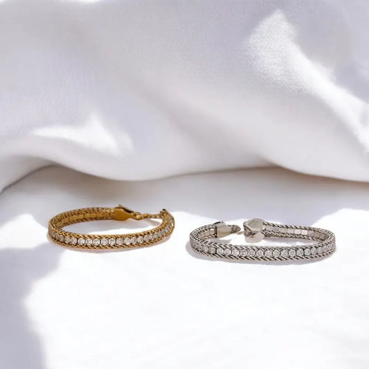 Two bracelets, one gold and one silver, on a white fabric background
