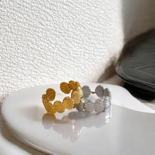 Gold and silver leaf-shaped rings on a white surface with a textured background