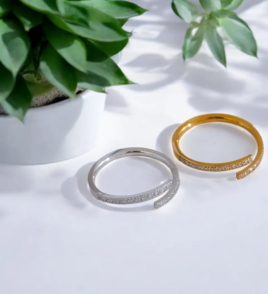 Two rings, one silver and one gold, on a white surface with green plants in the background.