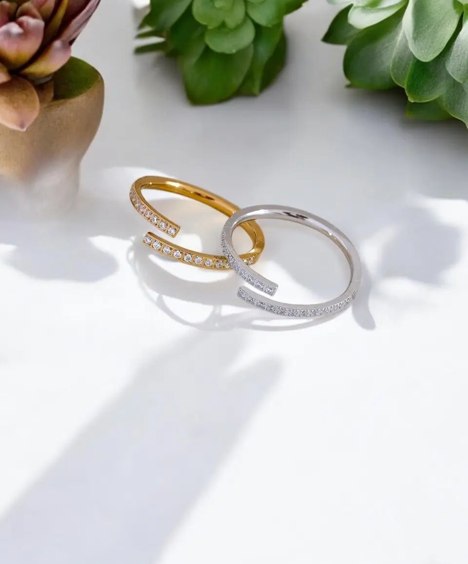 Two gold and silver rings on a white surface with green plants in the background.