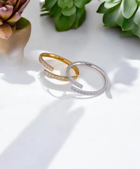 Two gold and silver rings on a white surface with green plants in the background.