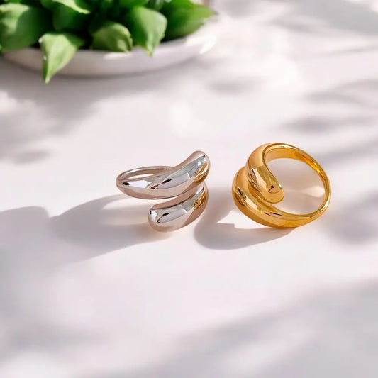 Two rings, one gold and one silver, on a light surface with a plant in the background.