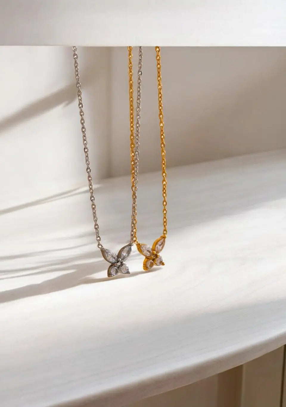 Two butterfly-shaped pendants on gold and silver chains against a white background