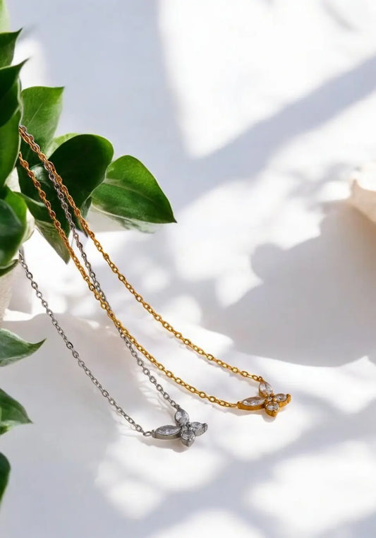 Two necklaces on a light surface with green leaves in the background