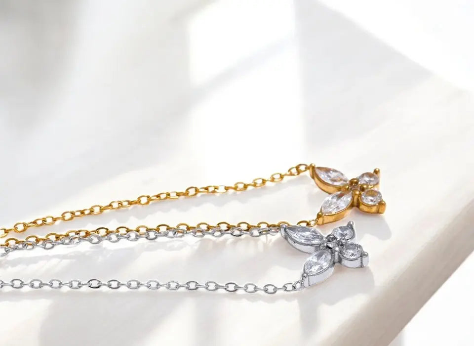 Two butterfly-shaped necklaces, one gold and one silver, on a light background.