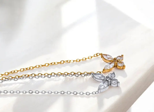 Two butterfly-shaped necklaces, one gold and one silver, on a light background.