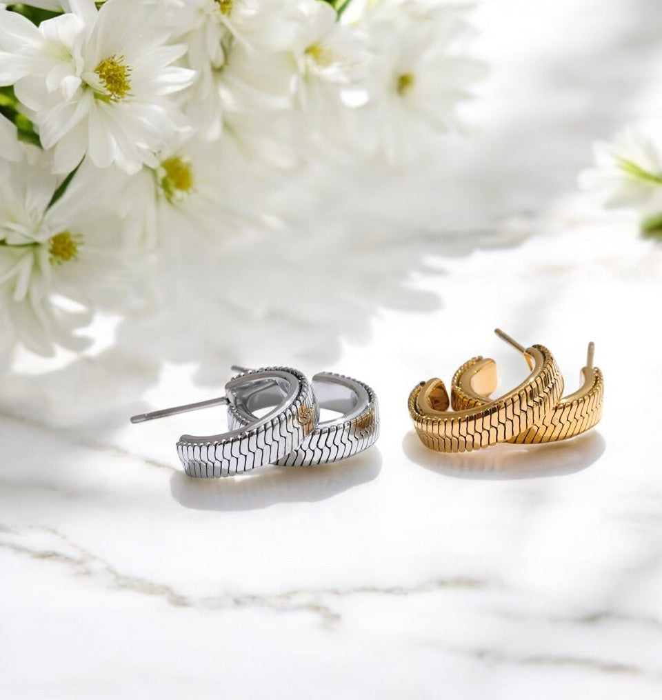 Pair of silver hoop earrings and gold hoop earrings on a white marble surface with white flowers in the background.