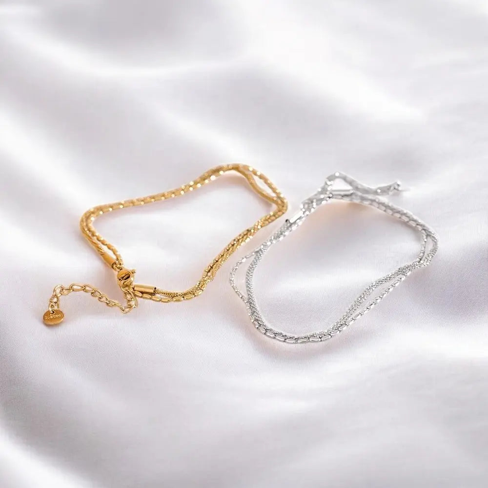 Gold and silver chain bracelets on a white fabric background