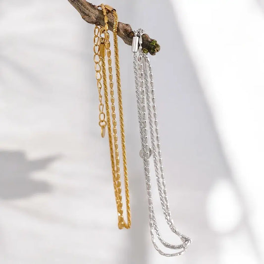 Two gold and silver necklaces hanging on a branch with a blurred white background