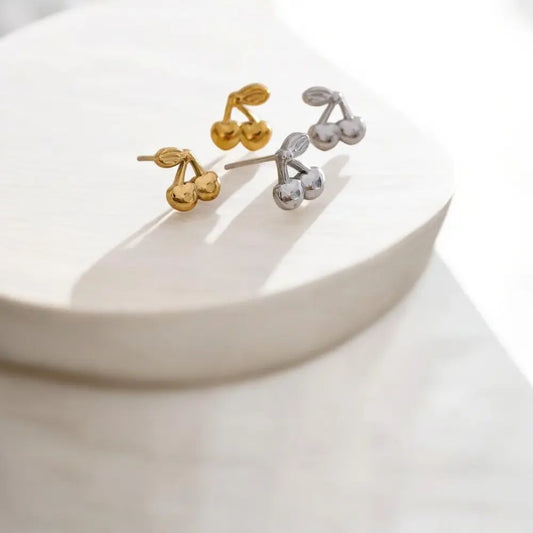 Gold and silver cherry-shaped earrings on a white surface