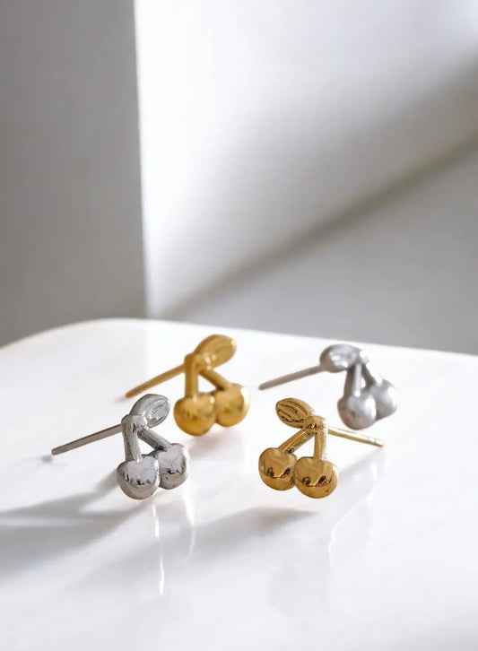 Cherry-shaped earrings in gold and silver on a white surface with a light background
