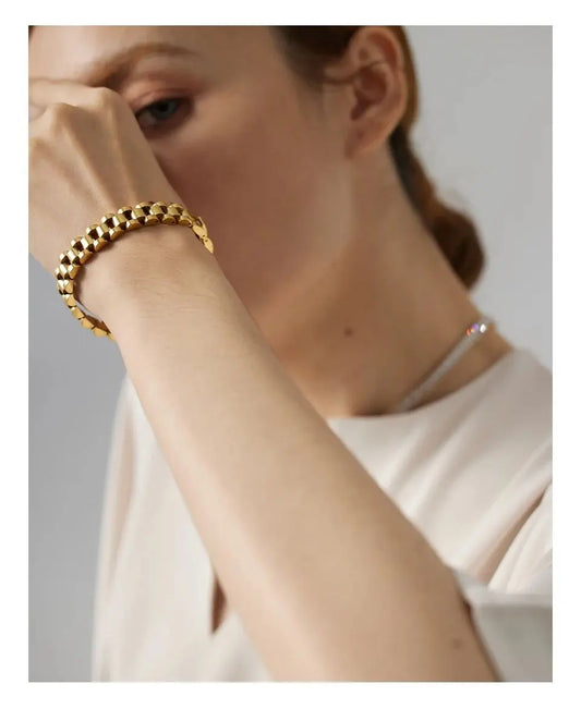 Person wearing a gold bracelet on a neutral background