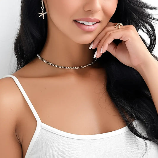 Woman wearing a silver necklace and earrings with a white top against a neutral background